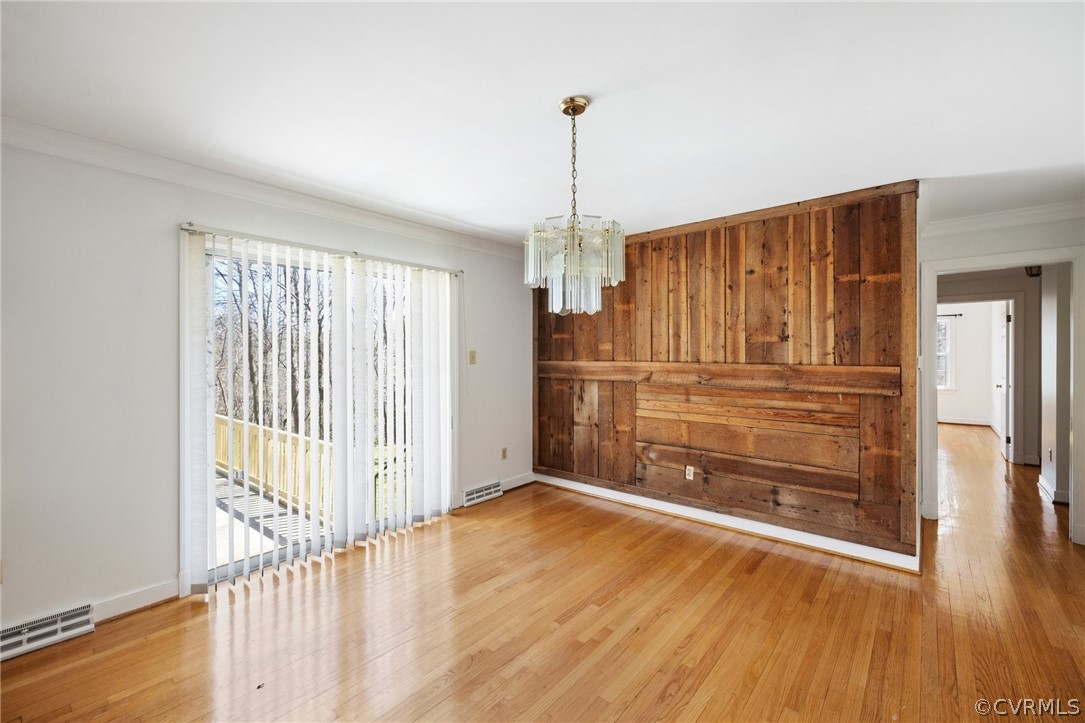 Spare room featuring a notable chandelier, a wealth of natural light, and light hardwood / wood-style floors