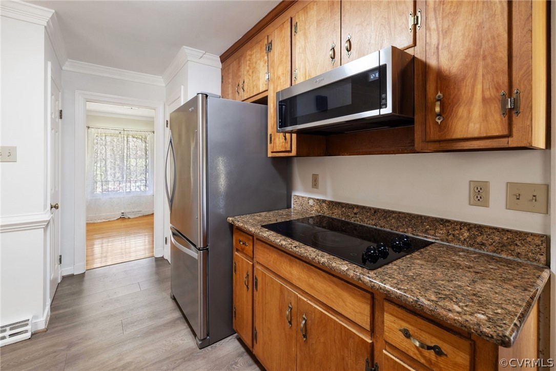 Kitchen featuring appliances with stainless steel finishes, crown molding, dark stone countertops, and light hardwood / wood-style floors