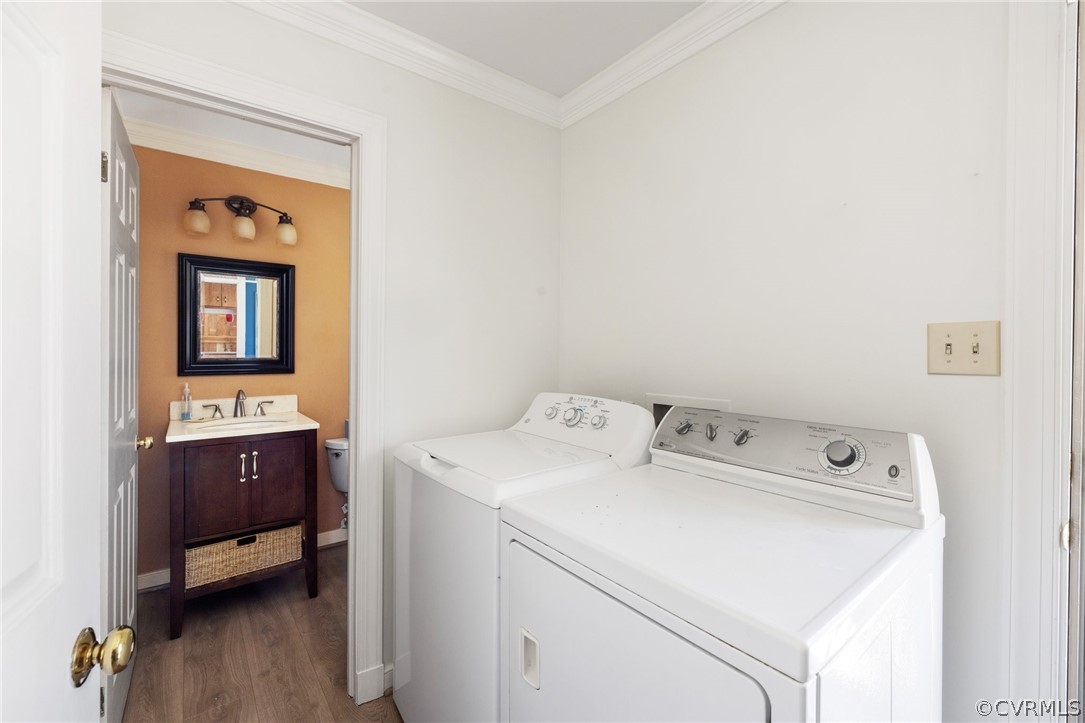 Laundry area with sink, ornamental molding, washer and dryer, and dark hardwood / wood-style flooring