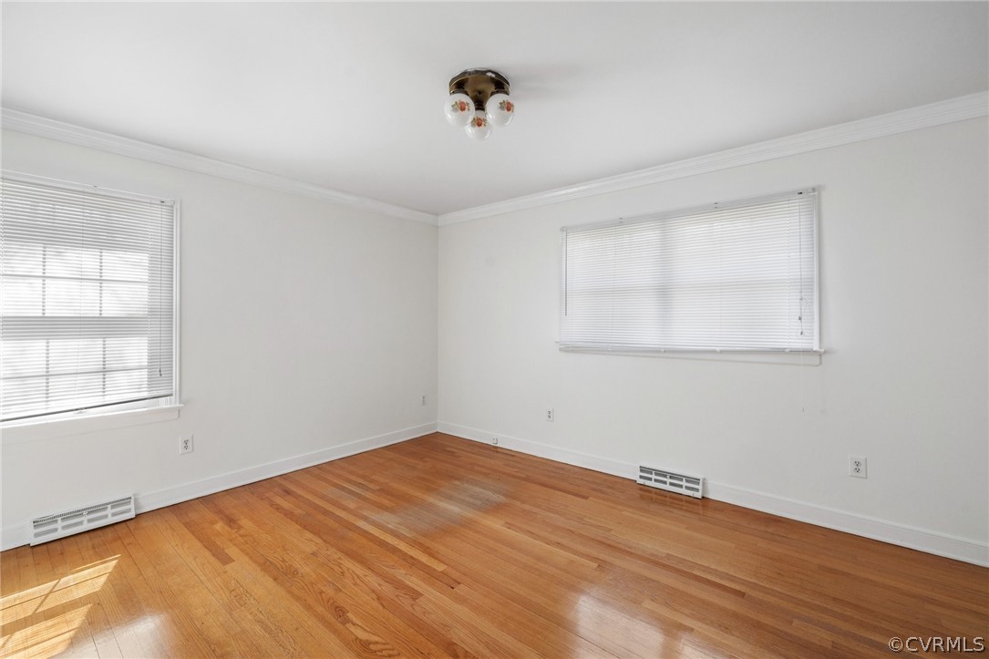 Empty room featuring ornamental molding and light wood-type flooring