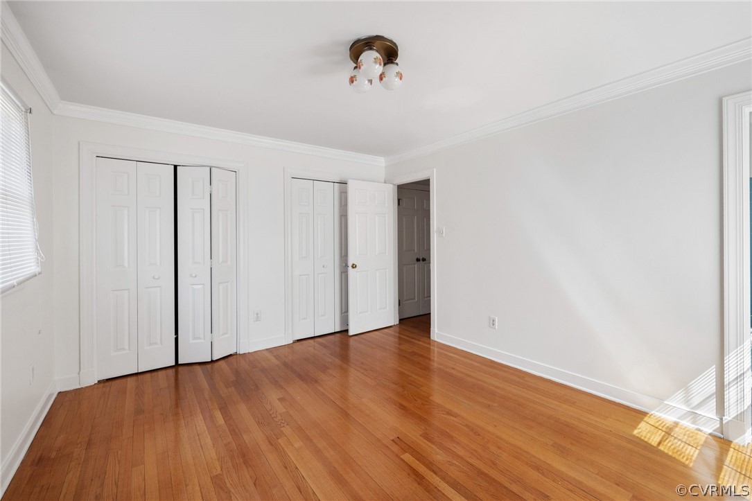 Unfurnished bedroom featuring crown molding, multiple closets, and hardwood / wood-style flooring