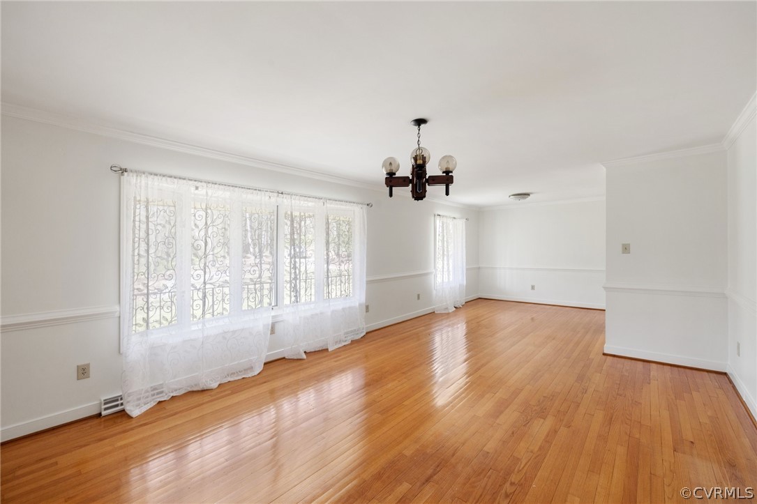 Empty room with crown molding, light wood-type flooring, and a chandelier