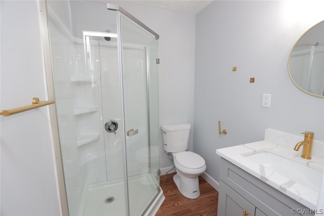 Bathroom with an enclosed shower, toilet, large vanity, and hardwood / wood-style floors