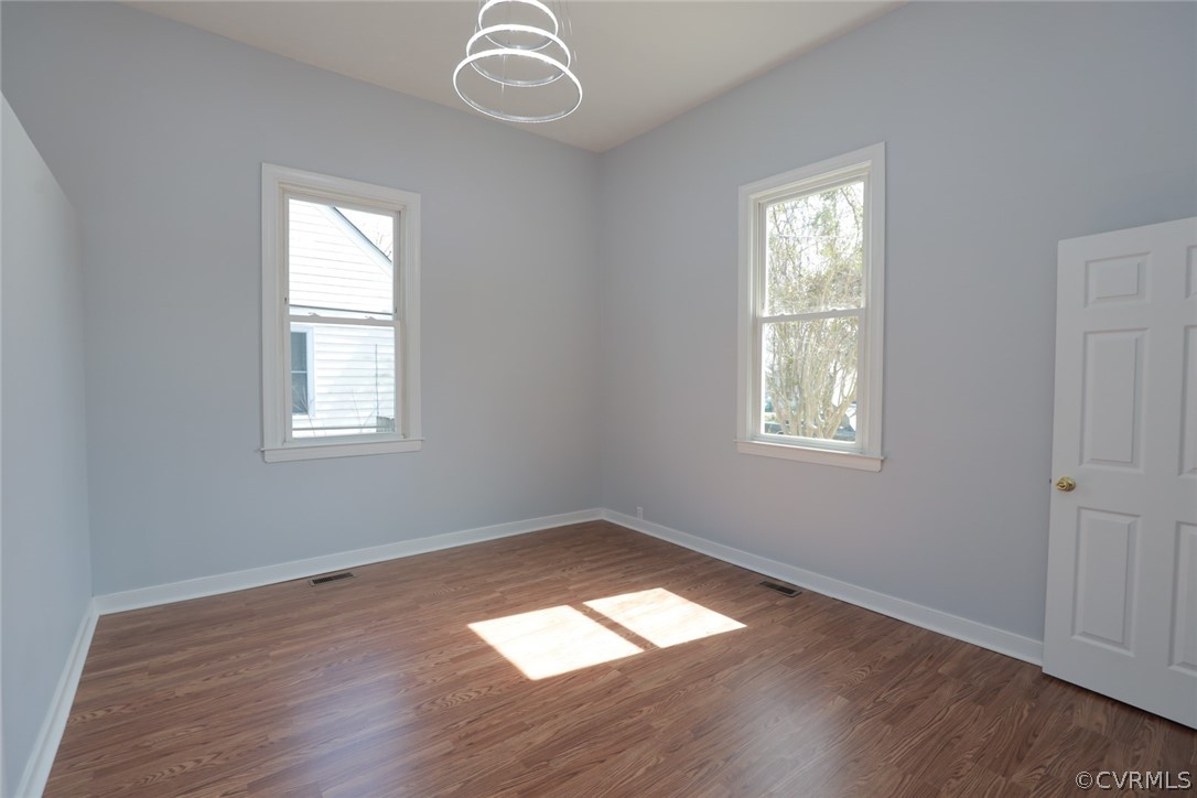 Spare room featuring a notable chandelier, a healthy amount of sunlight, and dark hardwood / wood-style floors