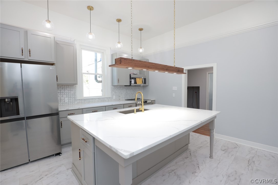 Kitchen with an island with sink, appliances with stainless steel finishes, backsplash, gray cabinets, and hanging light fixtures