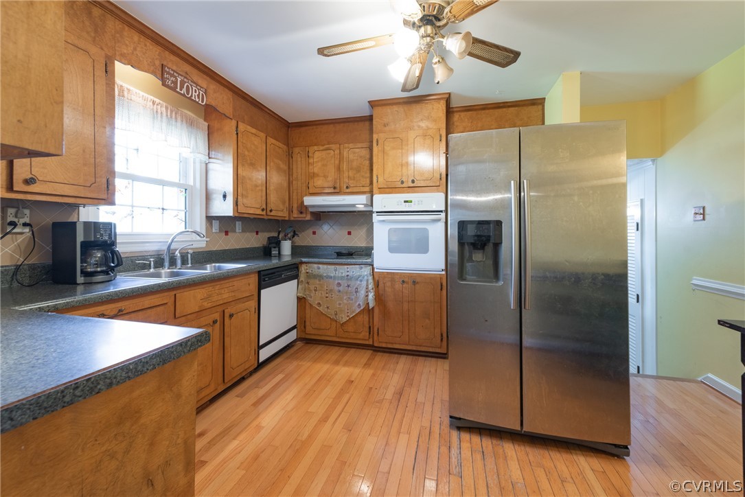 Kitchen with tasteful backsplash, ceiling fan, white appliances, sink, and light wood-type flooring