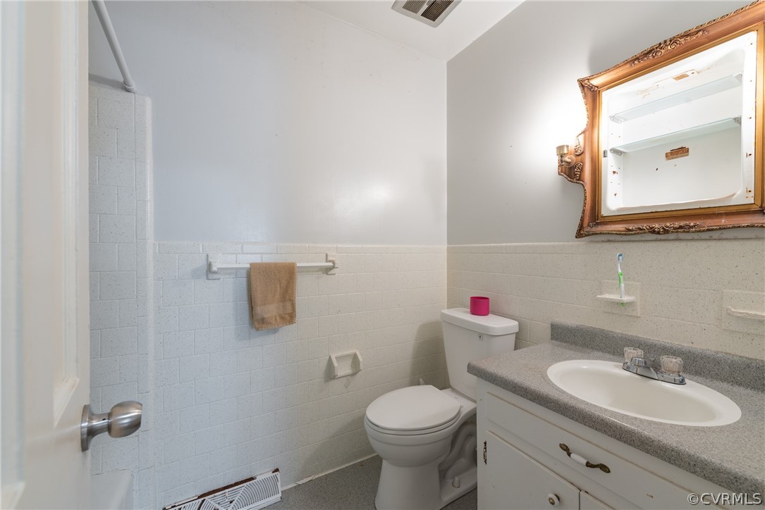 Bathroom with oversized vanity, toilet, tasteful backsplash, and tile walls