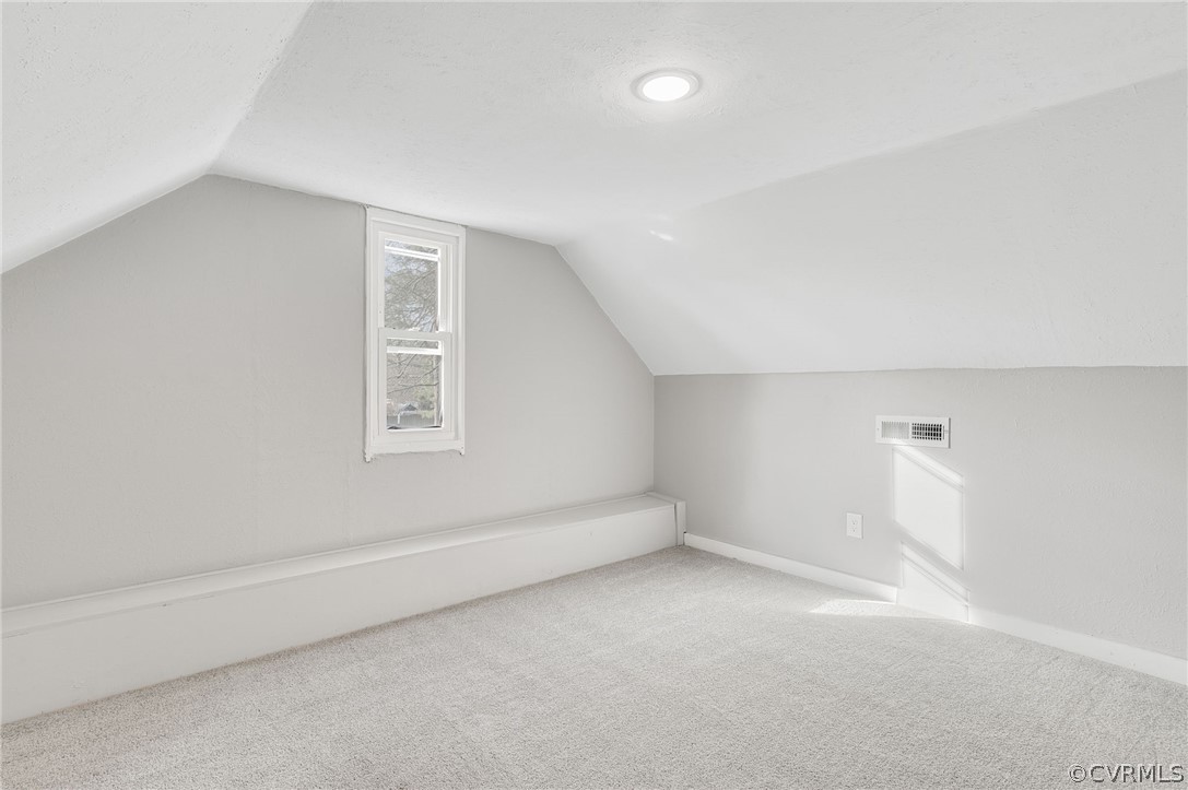 Bonus room with light colored carpet and vaulted ceiling