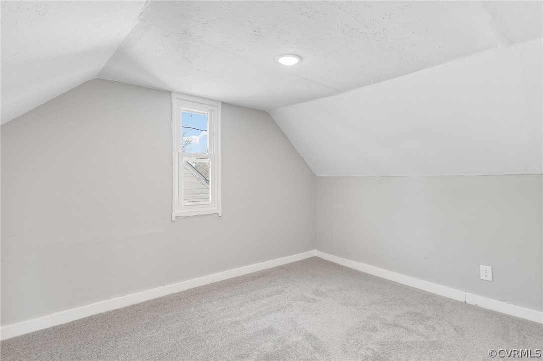 Bonus room with a textured ceiling, light carpet, and lofted ceiling