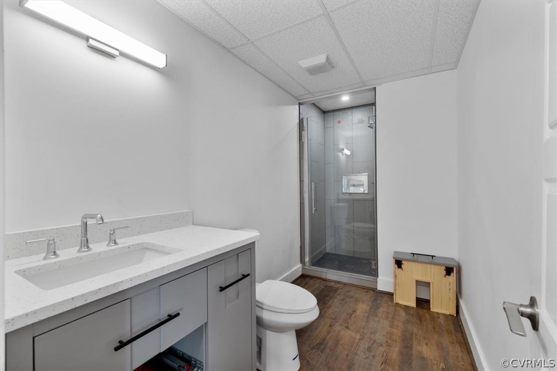 Bathroom featuring hardwood / wood-style floors, a drop ceiling, toilet, an enclosed shower, and vanity