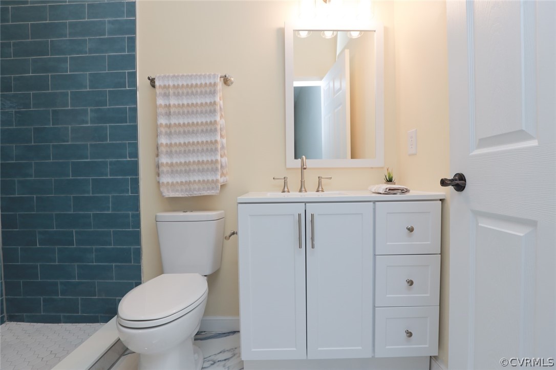 Bathroom with tiled shower, toilet, oversized vanity, and tile flooring