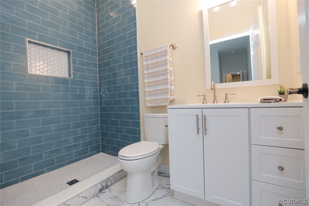 Bathroom with toilet, tile floors, vanity, and a tile shower