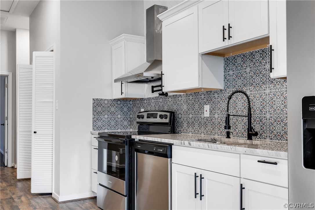 Kitchen featuring backsplash, wall chimney range hood, stainless steel dishwasher, range, and dark hardwood / wood-style flooring