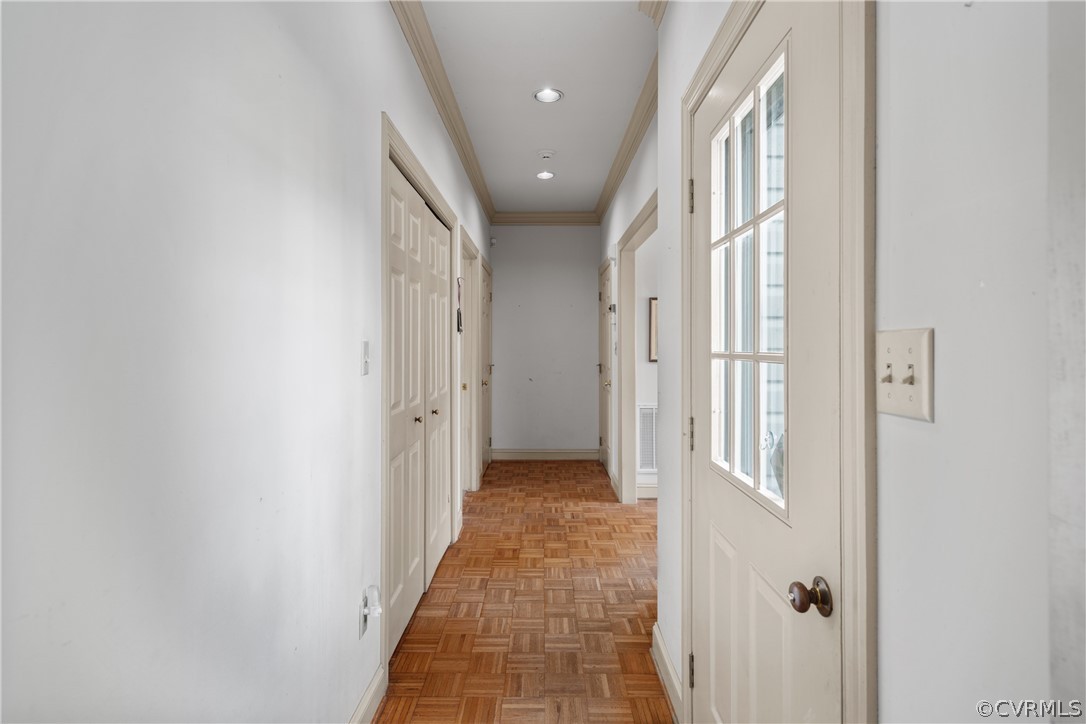 Hallway going to downstairs bedroom area with crown molding and dark parquet flooring