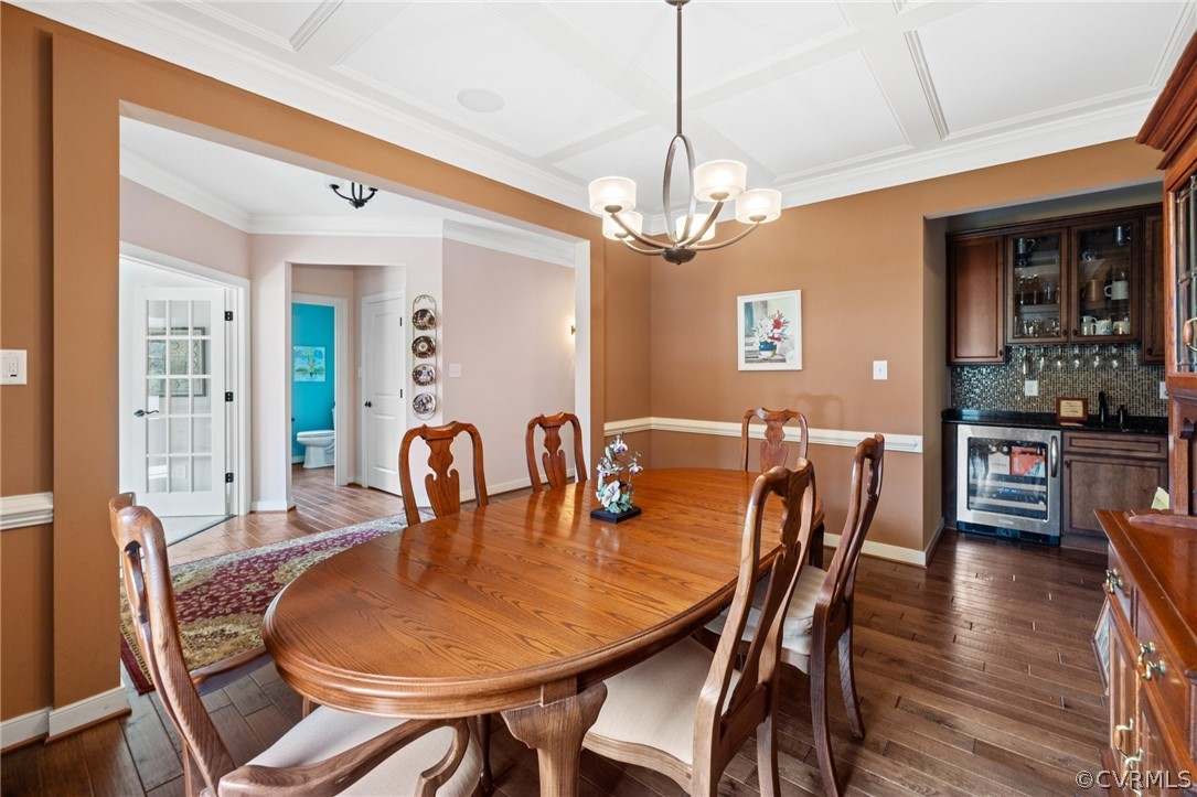 Dining area featuring ornamental molding, dark hardwood / wood-style floors, coffered ceiling, wine cooler, and a notable chandelier