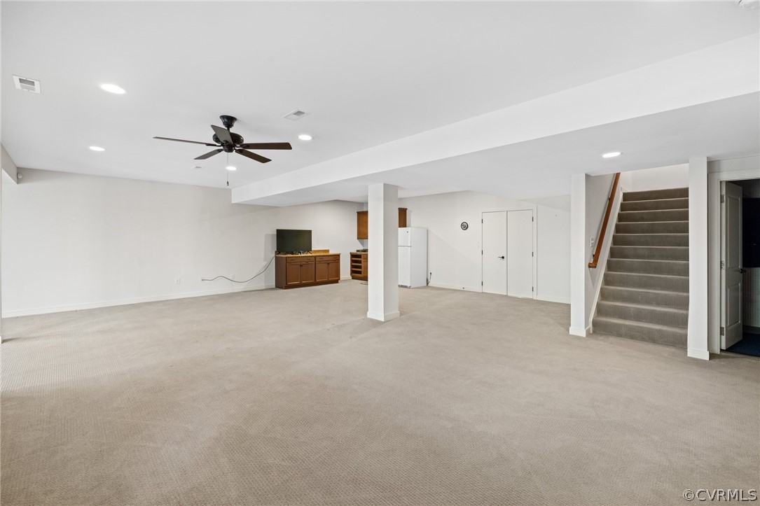 Basement with ceiling fan, white refrigerator, and light colored carpet