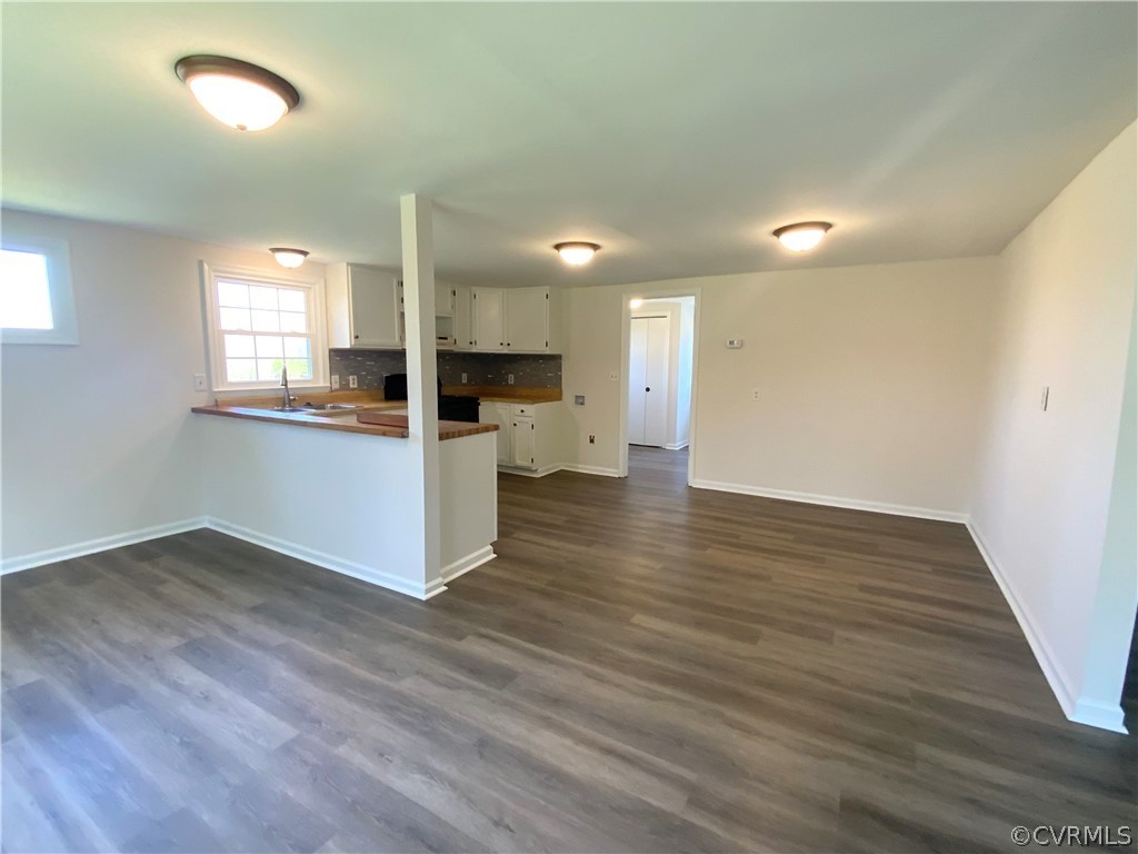 Kitchen featuring white cabinetry, kitchen peninsula, backsplash, and dark wood-type flooring