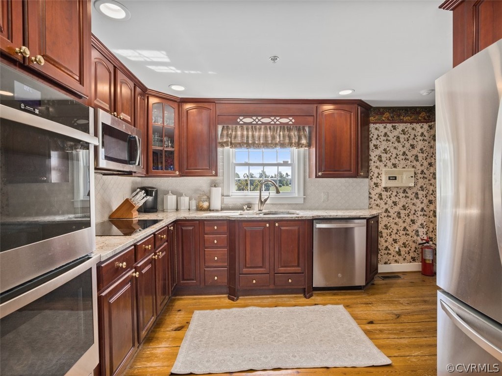 Kitchen with appliances with stainless steel finishes, light hardwood / wood-style flooring, sink, and light stone countertops