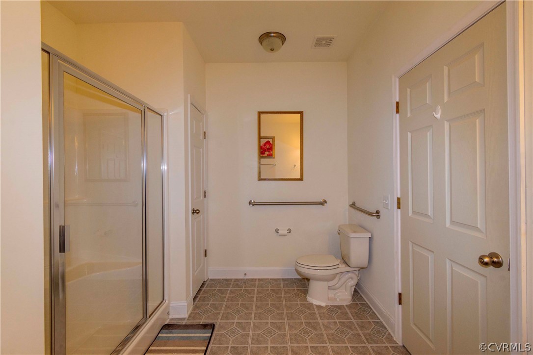 Bathroom with toilet, a shower with shower door, and tile floors
