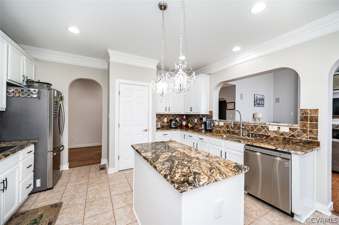 Kitchen with backsplash, dark stone countertops, appliances with stainless steel finishes, a kitchen island, and light wood-type flooring