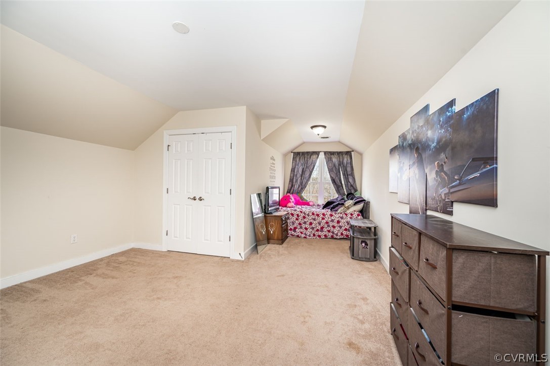 Bedroom with light colored carpet, lofted ceiling, and a closet