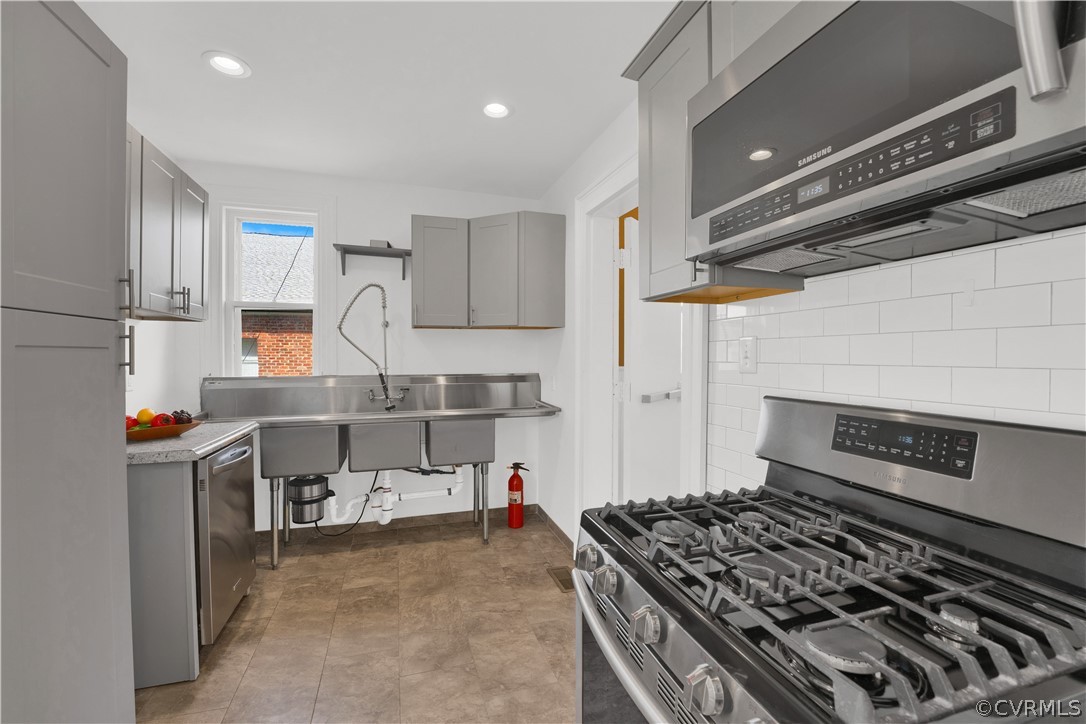 Kitchen featuring appliances with stainless steel finishes, tile flooring, gray cabinets, and backsplash