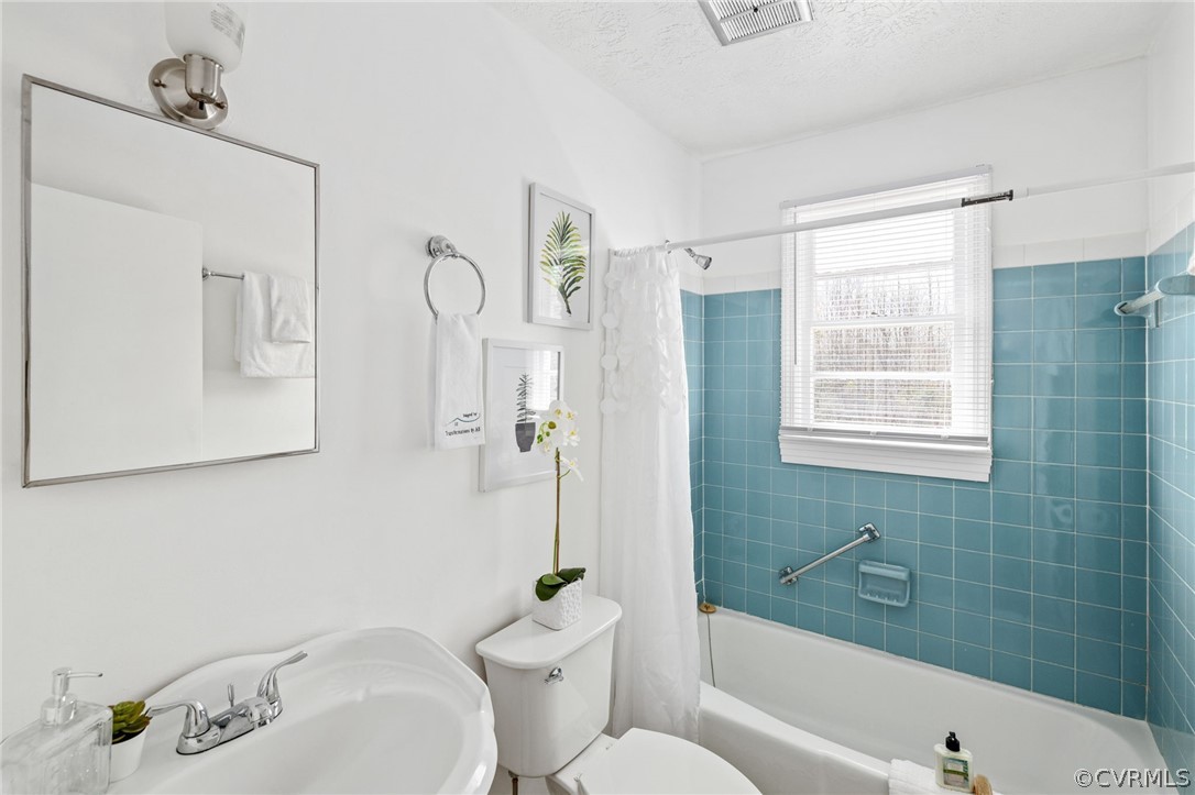 Full bathroom with sink, a textured ceiling, shower / tub combo with curtain, and toilet