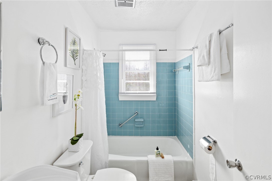 Bathroom featuring toilet, a textured ceiling, and shower / bath combo with shower curtain