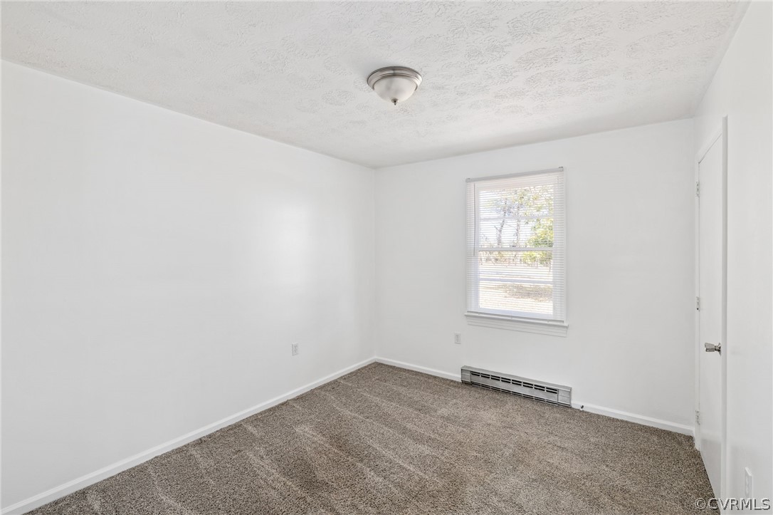 Unfurnished room with a baseboard heating unit, a textured ceiling, and dark colored carpet