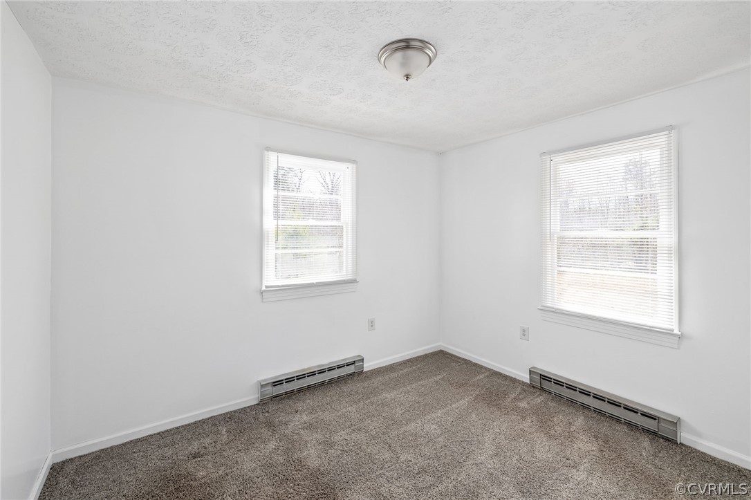 Carpeted empty room featuring a textured ceiling, a baseboard radiator, and plenty of natural light