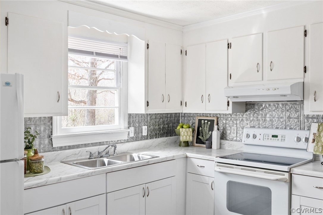 Kitchen with white cabinets, premium range hood, white appliances, and a healthy amount of sunlight