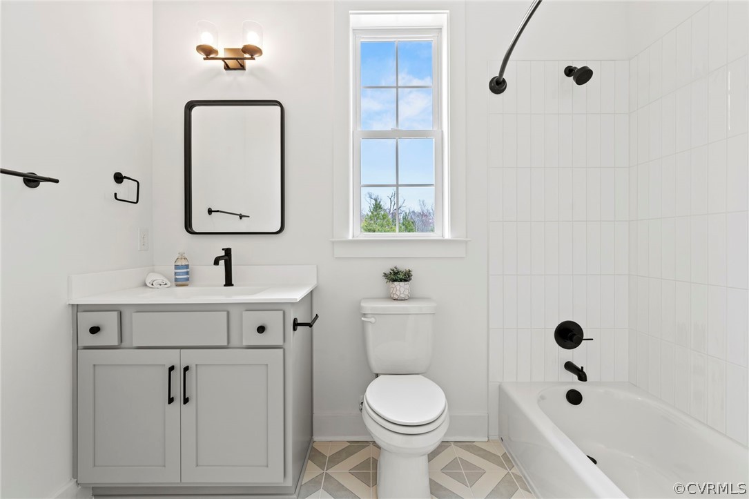 Full bathroom with tile floors, tiled shower / bath combo, toilet, and vanity