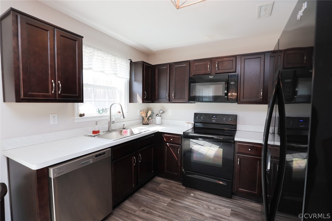 Kitchen with black appliances, sink, dark brown cabinets, and dark vinyl flooring