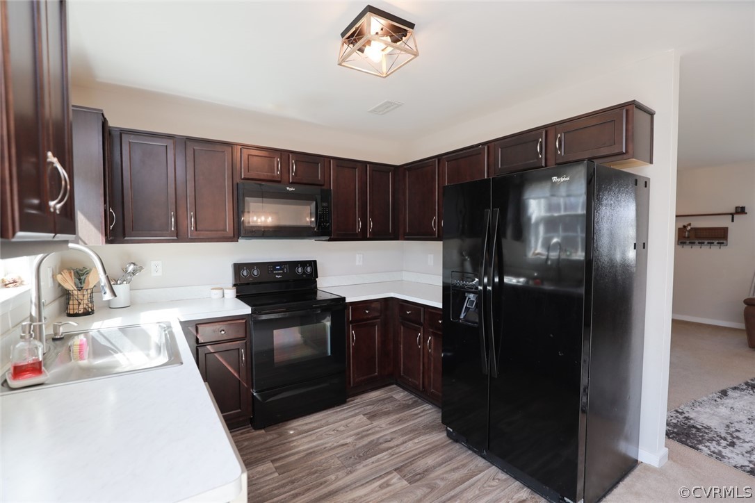 Kitchen with light vinyl flooring, dark brown cabinets, sink, and black appliances