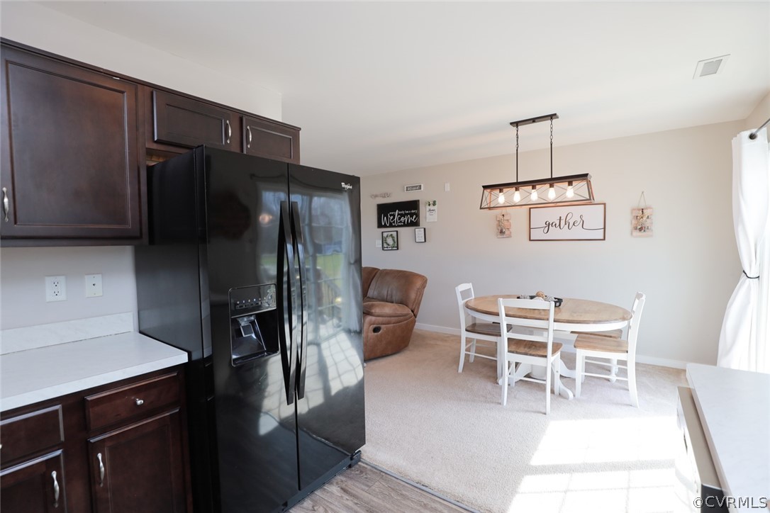 Kitchen with decorative light fixtures, light carpet, black fridge with ice dispenser, and dark brown cabinets