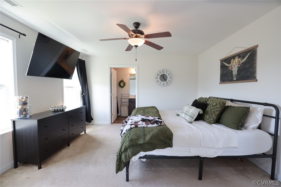 Bedroom with ensuite bathroom, light carpet, and ceiling fan