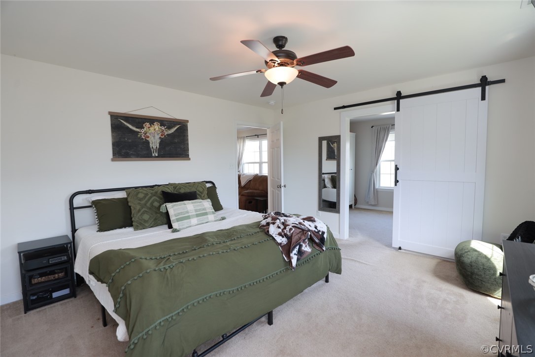 Bedroom with light colored carpet, a barn door, and ceiling fan