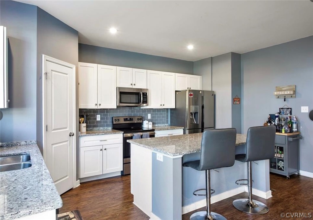 Kitchen with white cabinets, a breakfast bar, stainless steel appliances, dark wood-type flooring, and backsplash