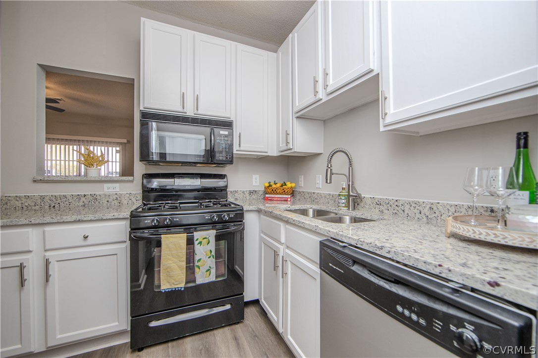 Kitchen featuring light stone counters, black appliances, sink, white cabinetry, and light hardwood / wood-style floors