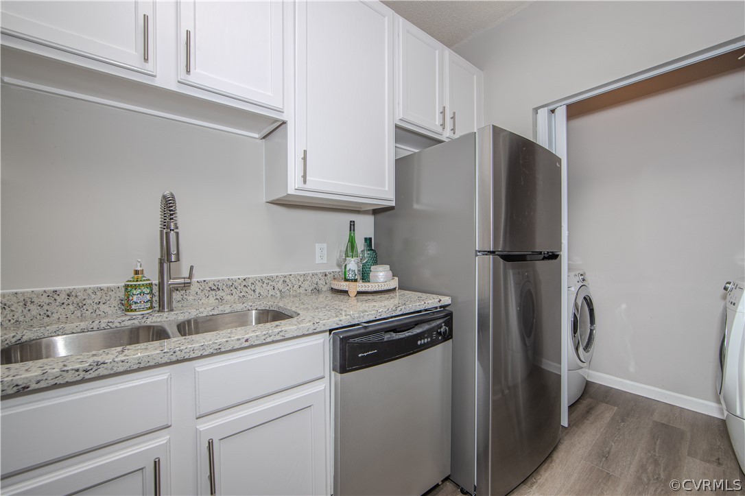 Kitchen with light stone counters, washer / clothes dryer, light hardwood / wood-style flooring, appliances with stainless steel finishes, and white cabinetry