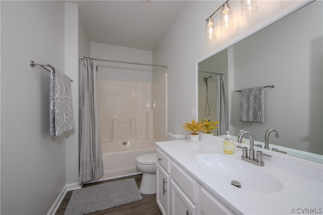 Full bathroom with toilet, shower / bath combo, vanity with extensive cabinet space, and hardwood / wood-style flooring
