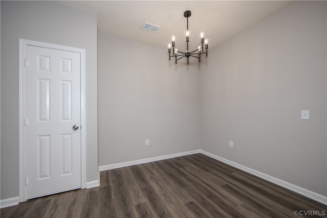 Empty room featuring a chandelier and dark hardwood / wood-style floors