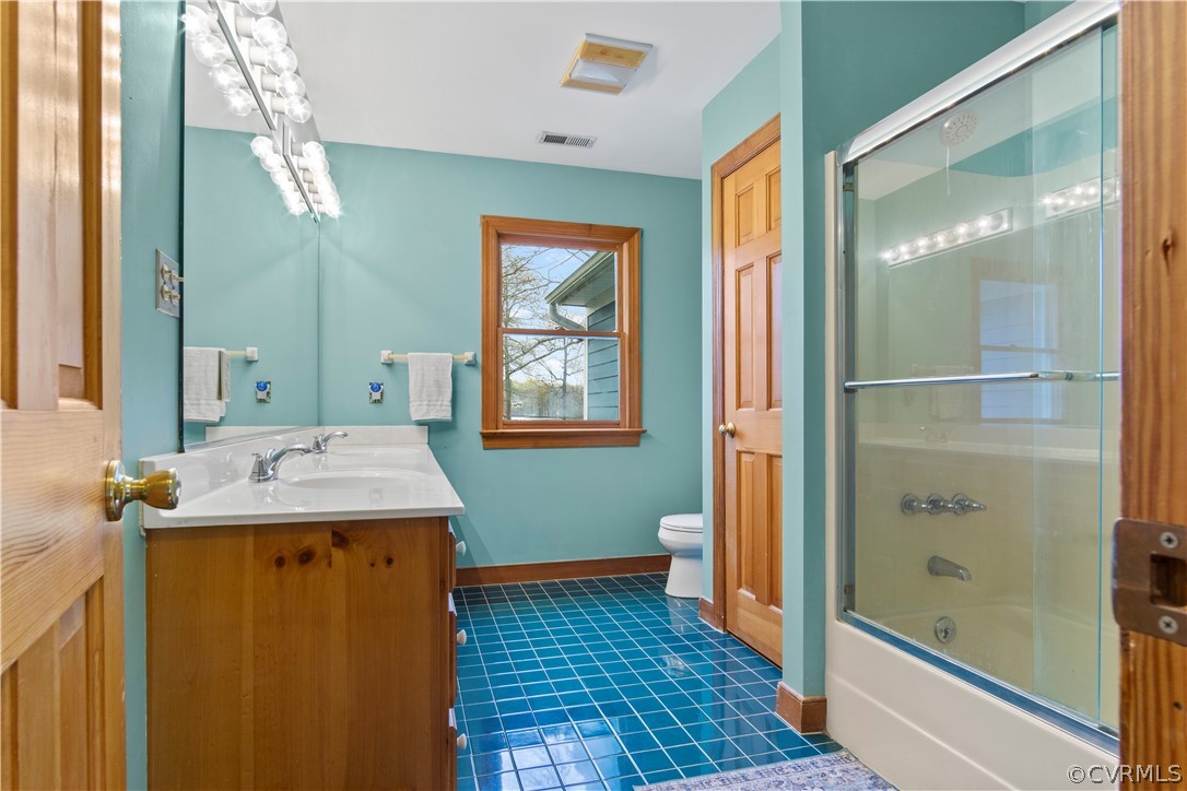 Full bathroom featuring bath / shower combo with glass door, tile floors, oversized vanity, and toilet