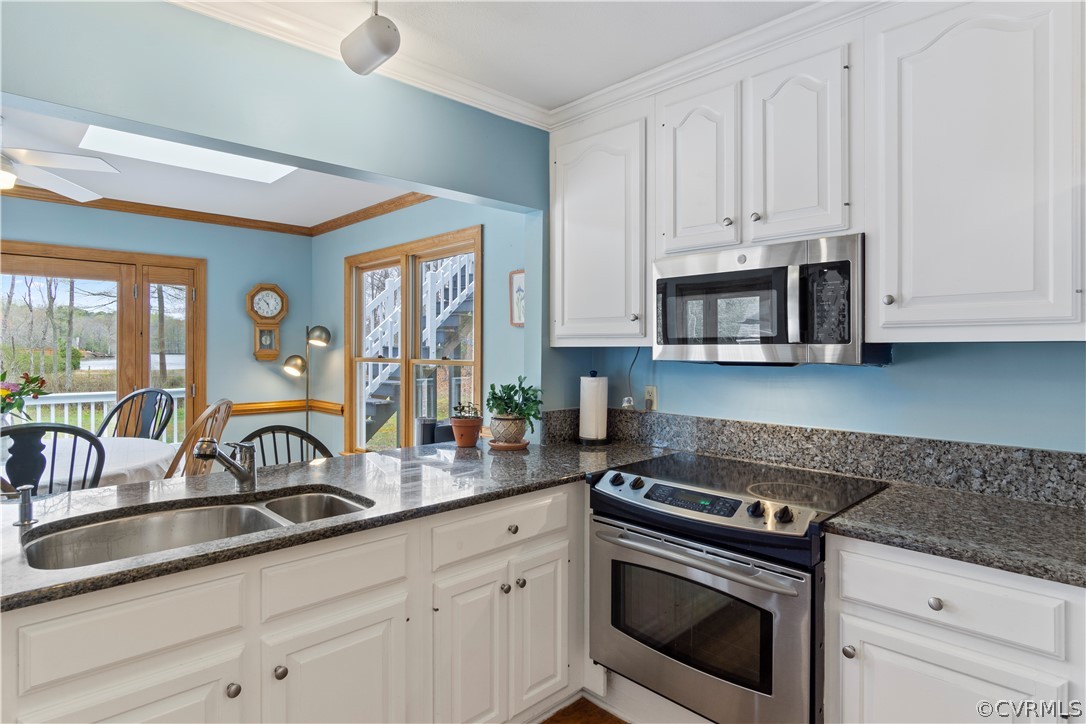 Kitchen featuring ceiling fan, sink, ornamental molding, white cabinets, and stainless steel appliances