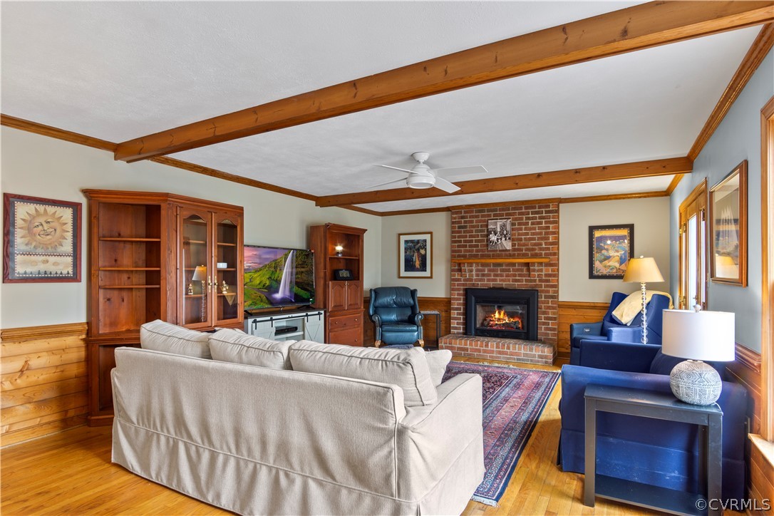 Living room with light hardwood / wood-style floors, brick wall, a brick fireplace, ceiling fan, and beamed ceiling