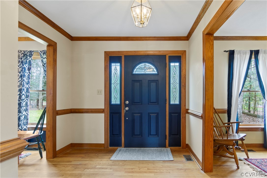Entryway with ornamental molding, a notable chandelier, and light hardwood / wood-style flooring