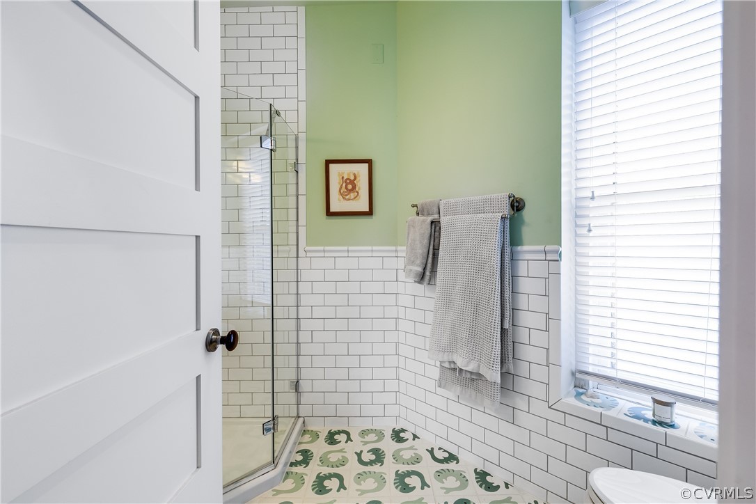 Bathroom featuring walk in shower, tile walls, and toilet
