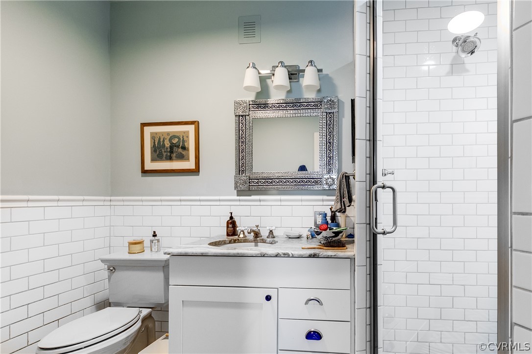 Bathroom with vanity, tile walls, a shower with shower door, toilet, and tasteful backsplash