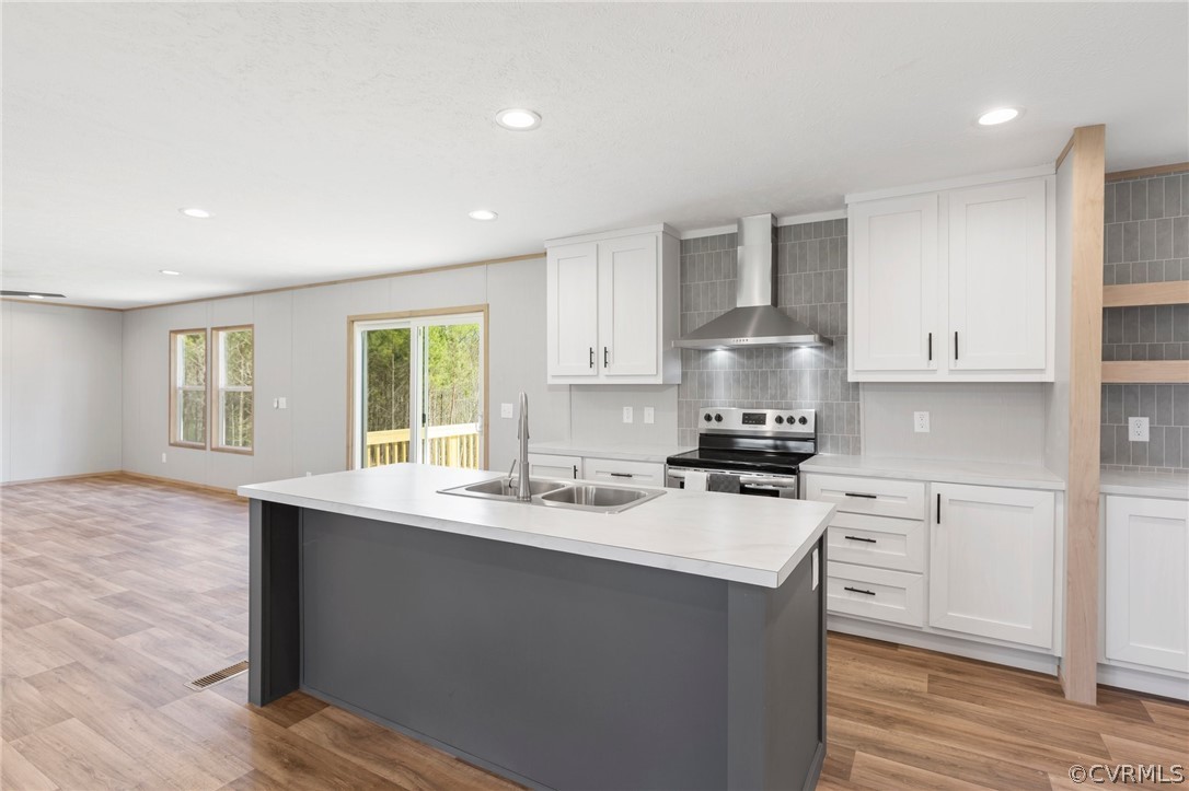 Kitchen featuring a center island with sink, stainless steel electric range oven, light wood-type flooring, wall chimney exhaust hood, and sink