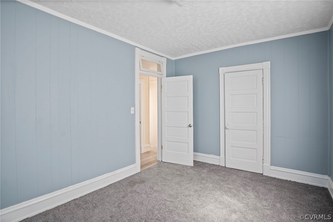 Unfurnished bedroom with a textured ceiling, ornamental molding, and carpet flooring